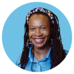 Porträttbild av Ruth Kizza Bohlin, specialist i psykiatri på ADHDonline. Kvinna med mörka lockar och färgglatt pärlat hårband, bär ljusblå skjorta och dekorativa örhängen, med ett varmt leende.